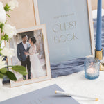 Wedding guest book sign with photo of couple and blue candle on a table.