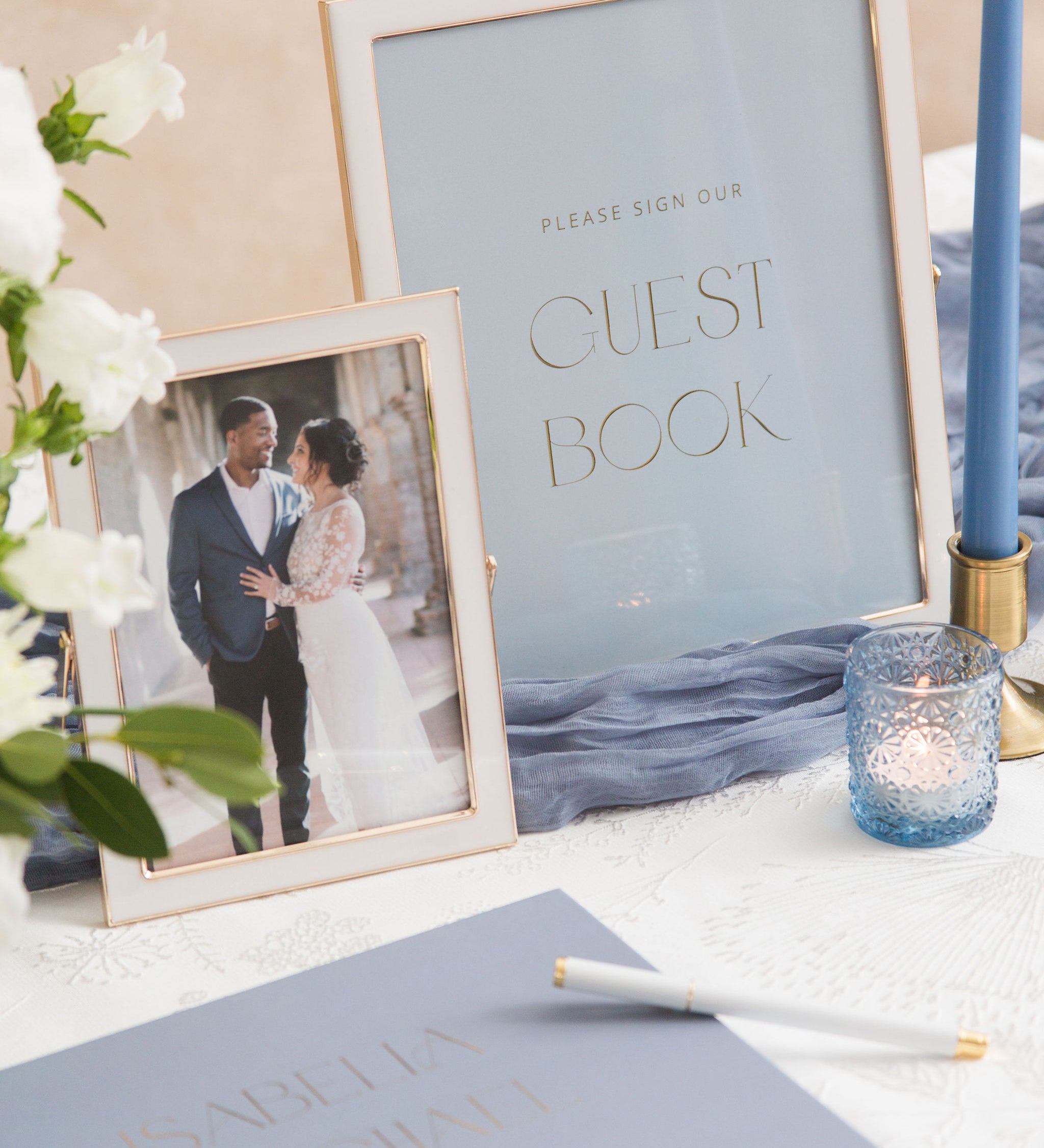 Wedding guest book sign with photo of couple and blue candle on a table.