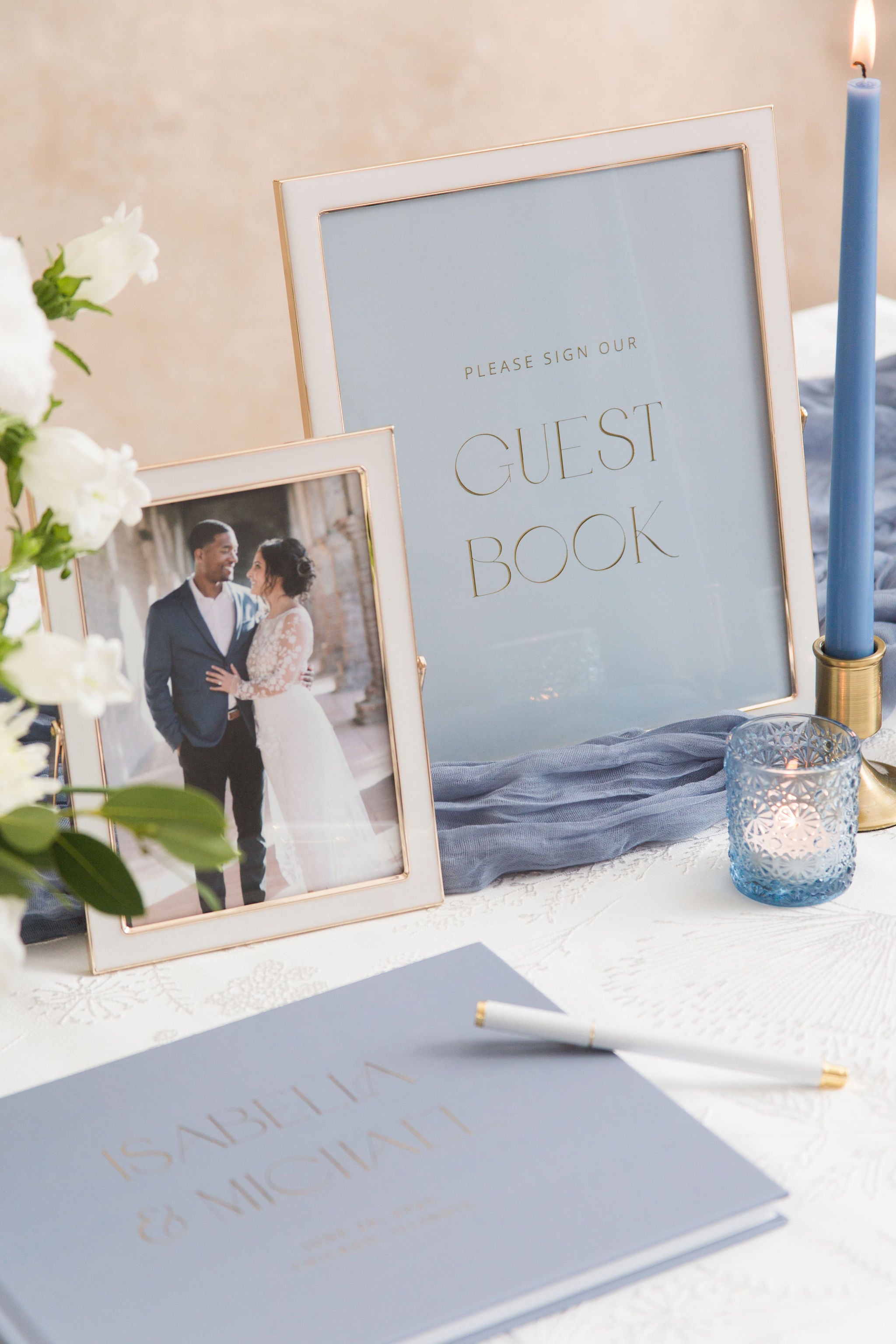 Wedding guest book sign with photo of couple and blue candle on a table.